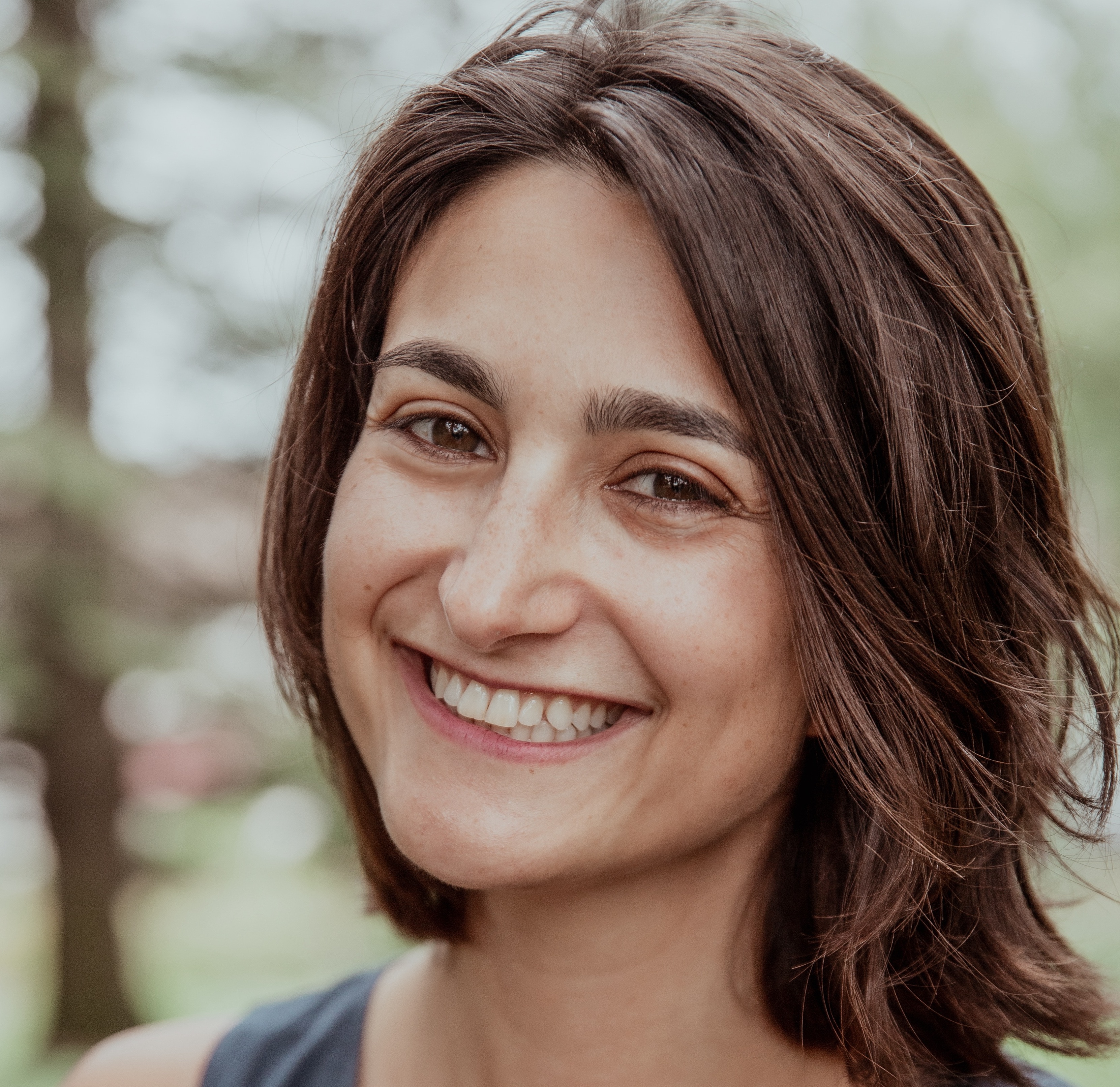 Tessa Bridge, a coach for nonprofit leaders, smiling warmly at the camera in natural outdoor lighting.