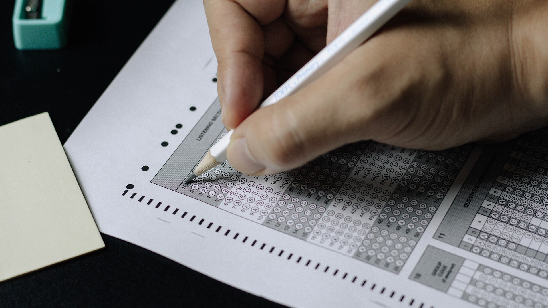 A hand with a pencil filling in a multiple choice exam sheet